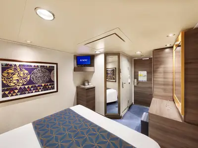 Moderne Aussenkabine an Bord der MSC Divina. Mit Doppelbett, Kunstwerk, Fernseher, Schminktisch und Ganzkörperspiegel. Helle und einladende Raumgestaltung mit blauer Tagesdecke und blauem Teppich.