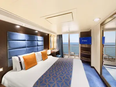 Moderne Balkonkabine an Bord der MSC Divina. Doppelbett mit blauer Kopflehne, orangefarbenen Kissen und einem Balkon mit weitem Meerblick. TV mit MSC Logo.