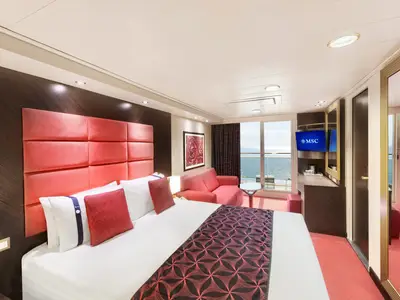 Eine helle Premium Balkonkabine an Bord der MSC Divina mit rotem Doppelbett, Sofa und Meerblick von der privaten Veranda. Die Kabine ist modern und elegant eingerichtet.