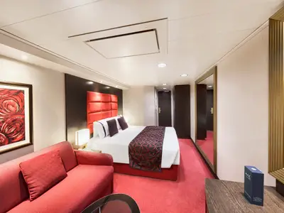 Blick in eine modern und elegant eingerichtete Balkonkabine an Bord der MSC Divina mit rotem Teppich, rotem Sofa und grossem Doppelbett.