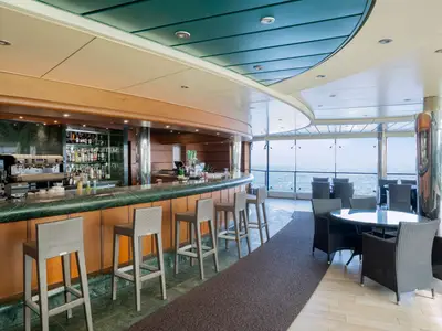Elegante Bar 'Le Sirene' an Bord der MSC Divina. Grüne Theke mit Hockern und Getränkeauswahl. Lounge-Bereich mit Tischen und Sesseln. Große Fenster bieten weiten Meerblick.
