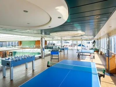 Heller Spielbereich an Bord der MSC Divina mit Tischfussball- und Tischtennisplatten auf Holzboden. Blick auf Aussendeck.