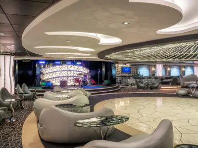 Die moderne Black & White Lounge an Bord der MSC Divina, mit eleganter Bestuhlung, einer beleuchteten Bühne mit Schlagzeug und einer auffälligen Tanzfläche.