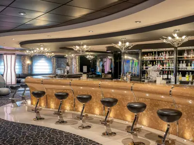 Die elegante Black & White Bar an Bord der MSC Divina. Ein geschwungener Bartresen mit Hockern und ein voll bestücktes Spirituosenregal sind sichtbar. Moderne Beleuchtung prägt das luxuriöse Ambiente.
