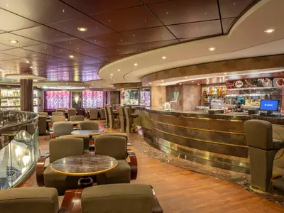 Blick auf das Caffè Italia an Bord der MSC Divina mit einer geschwungenen Bar und vielen Sitzgelegenheiten. Der Raum ist elegant gestaltet mit dunklen Holz- und Marmorelementen, sowie indirekter Beleuchtung. Eine gemütliche Atmosphäre ohne Personen.