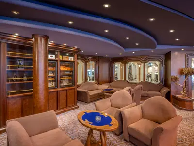 Innenansicht der eleganten Zigarren-Lounge an Bord der MSC Divina. Bequeme beigefarbene Sessel, dunkle Holzregale mit Spirituosen und Zigarrenvitrinen prägen den Raum. Die moderne Decke ist geschwungen.