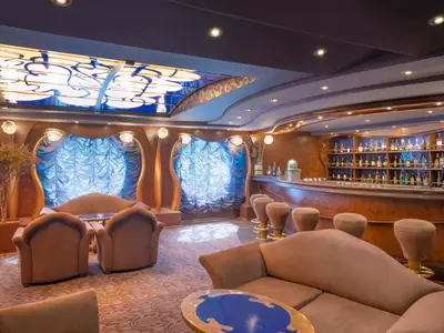 Blick in die elegante Bar-Lounge 'The Cigar Lounge' an Bord der MSC Divina mit einer langen, geschwungenen Bar, Hockern und mehreren Sitzgruppen aus bequemen Sesseln und Sofas. Die Inneneinrichtung ist luxuriös und warm.