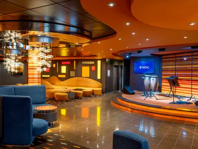 Innenansicht der eleganten Golden Jazz Bar an Bord der MSC Divina. Man sieht moderne Sitzbereiche, eine beleuchtete Bühne mit Musikinstrumenten und einen beeindruckenden Kronleuchter.