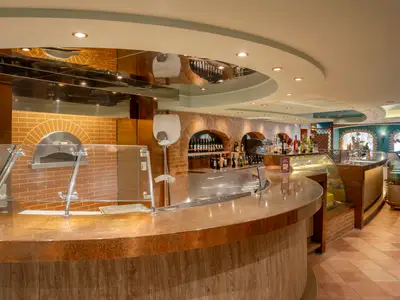 Innenansicht der Pizzeria La Cantina di Bacco an Bord der MSC Divina. Zu sehen sind ein Pizzaofen, eine lange Theke, Weinregale und gemuetliche Sitzbereiche in warmer Beleuchtung.