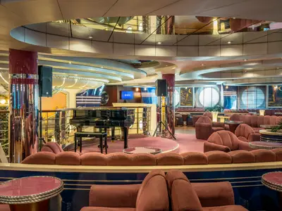 Innenansicht der eleganten La Luna Bar-Lounge an Bord der MSC Divina mit rotem Teppich, plueschigen Sitzen, Klavier, Bar und Bullaugenfenstern.