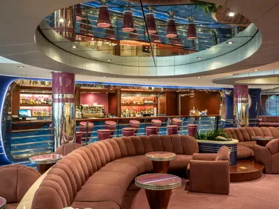 Elegante La Luna Bar an Bord der MSC Divina. Geschwungene rosafarbene Sofas, runde Tische, gut bestückte Bar mit Hockern. Moderne glänzende Oberflächen und blaue Akzente.