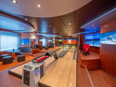 Die moderne Bowlingbahn der MSC Divina mit roten Kugeln. Komfortable Sitzbereiche, mehrere Bildschirme mit Sportvideos und eine rote Vespa als Blickfang prägen den Raum.