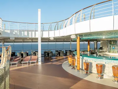 Die Outdoor-Bar Poseidon auf der MSC Divina lädt mit bequemen Stühlen, Tischen und Sonnenliegen zum Entspannen ein. Im Hintergrund das weite Meer.
