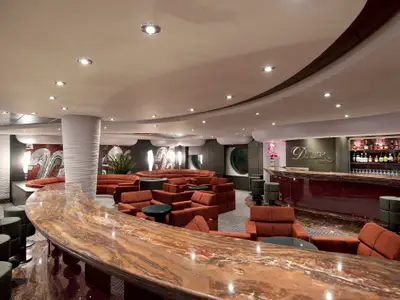 Weitwinkelaufnahme der Divina Bar an Bord der MSC Divina mit runder Marmortheke, roten Lounge-Sesseln und Flaschenregal. Indirekte Beleuchtung schafft eine gemütliche Atmosphäre.