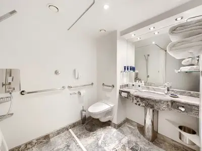 Barrierefreies Bad an Bord der MSC Divina mit begehbarer Dusche, Haltegriffen, wandmontierter Toilette und Waschtisch. Marmorboden und grosser Spiegel.