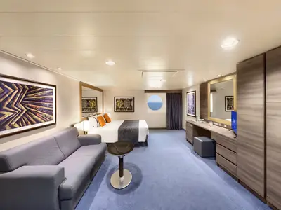 Helle, barrierefreie Aussenkabine der MSC Divina. Mit Doppelbett, Sofa, Schreibtisch und rundem Bullauge zum Meer. Moderne Einrichtung in Holz- und Blautönen.