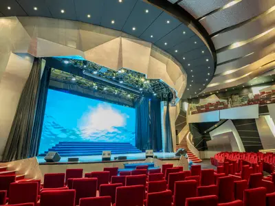Das Pantheon Theatre an Bord der MSC Divina. Rote Sitze, eine große Bühne mit blauem LED-Bildschirm, ein Balkon und eine Wendeltreppe sind sichtbar.