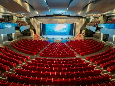 Blick in das Pantheon Theater an Bord der MSC Divina. Der leere Saal mit roten Sitzen und Buehne. Eine LED-Leinwand zeigt eine Unterwasser-Szene. Moderne Architektur.