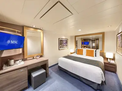 Eine helle Innenkabine an Bord der MSC Divina mit einem grossen Doppelbett, einem Flachbildfernseher, einem Schminktisch mit Spiegel und einer Minibar.