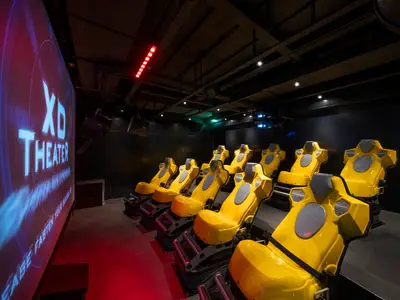 An Bord der MSC Divina ist ein XD Theater mit Reihen gelber dynamischer Sitze und einer grossen Leinwand, die 'XD Theater' anzeigt.