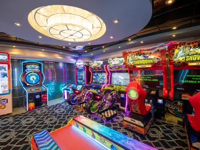 Bunte und lebhafte Spielhalle an Bord der MSC Divina mit verschiedenen Arcade-Spielen, darunter Motorrad-Simulatoren und Rennspiele mit hellen Neonlichtern und einem großen Kronleuchter an der Decke.