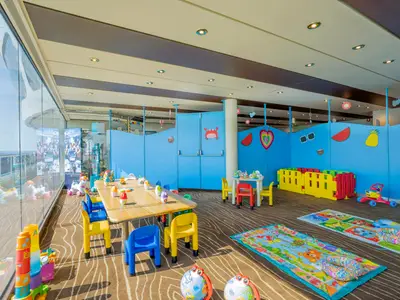 Der bunte Kinderbereich an Bord der MSC Divina. Er hat kleine Tische, Stühle und viel Spielzeug. Weiche Spielmatten liegen auf dem Teppichboden. Große Fenster bieten Meerblick.