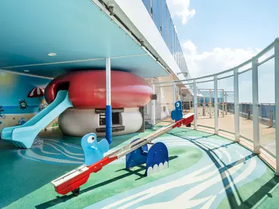 Bunter Kinder-Spielbereich Doremiland an Bord der MSC Divina mit Rutsche, Wippe und Wandbildern. Im Hintergrund das Meer.