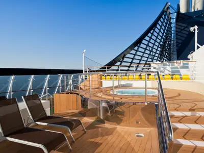 Das Sonnendeck der MSC Divina mit Teakholz-Boden, braunen Liegestühlen, einem Whirlpool, Volleyballnetz und Basketballkorb. Im Hintergrund das blaue Meer.