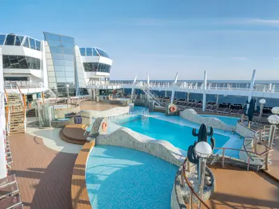 Blick auf den Aquapark der MSC Divina an einem sonnigen Tag. Mehrere hellblaue Pools, Whirlpools, braune Holzdecks und die moderne Glasarchitektur des Schiffes sind zu sehen. Keine Personen.