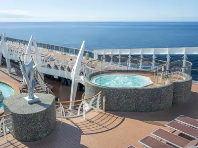 Das sonnige Sonnendeck der MSC Divina mit einem sprudelnden Whirlpool und einer modernen Skulptur. Im Hintergrund ist das weite, blaue Meer sichtbar. Liegestühle auf Holzdeck.