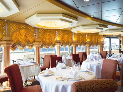 Das elegante Le Muse Restaurant der MSC Divina. Goldene Vorhänge, weiß gedeckte Tische mit Besteck und roten Stühlen. Große Fenster mit Meerblick. Keine Personen.