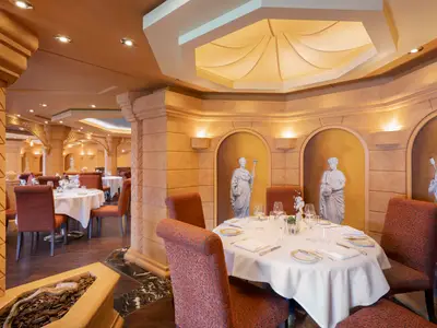 Blick in das elegant gedeckte Restaurant 'Le Muse' mit Marmorstatuen in Nischen und warmem Licht an Bord der MSC Divina.
