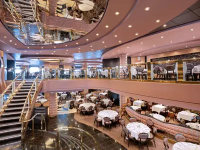 Das elegante, mehrstöckige Restaurant an Bord der MSC Divina. Zahlreiche gedeckte Tische und Stühle sind auf verschiedenen Ebenen angeordnet. Eine breite Treppe mit goldenen Geländern führt nach unten. Die Decke ist verspiegelt.