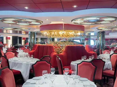 Blick in das elegante Restaurant Villa Rossa an Bord der MSC Divina. Rote Samtstühle, weiss gedeckte Tische und eine opulente goldene Deckenleuchte dominieren den luxuriösen Raum.