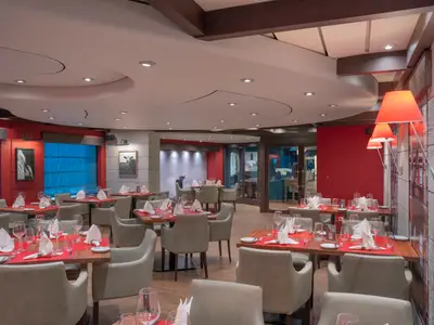 Restaurant Butcher's Cut an Bord der MSC Divina: gedeckte Holztische mit roten Platzsets, Gläsern, grauen Stühlen. Rote Wände mit Kunst und Deckenbeleuchtung. Keine Personen.