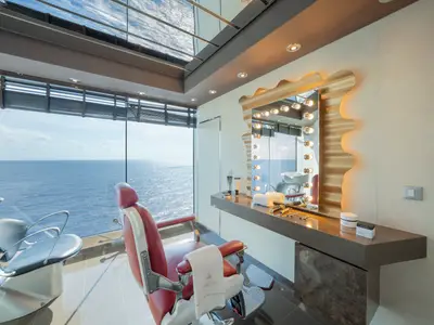 Eleganter Barbershop im MSC Aurea Spa an Bord der MSC Divina mit Meerblick. Roter Friseurstuhl, goldener Spiegel mit Lichtern und Pflegeprodukten.