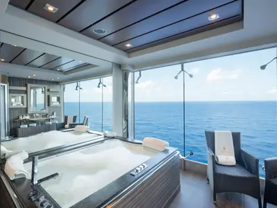 Luxuriöser Spa-Bereich an Bord der MSC Divina mit grosser Badewanne, die Meerblick bietet. Rechts sind Rattanstühle mit weissen Handtüchern zu sehen. Die Decke ist modern gestaltet.