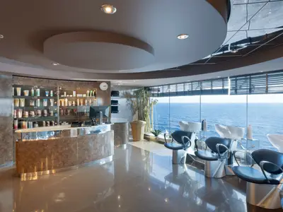 Der moderne Friseursalon im MSC Aurea Spa an Bord der MSC Divina mit grossen Fenstern, die einen weiten Blick auf das Meer ermöglichen. Vorne sind mehrere Frisierstühle und Waschbecken zu sehen, hinten eine Rezeption und Produktregale.