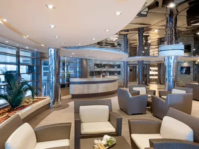 Moderne Spa-Lounge an Bord der MSC Divina. Heller Marmortresen, Korbsessel, Pflanzen, Fenster und eine spiegelnde Decke. MSC Aurea Spa-Schild.