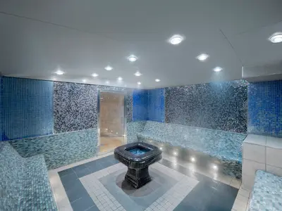 Blick in den Thermalbereich des MSC Aurea Spa an Bord der MSC Divina. Blaue Mosaikfliesen, geschwungene Bänke und ein zentrales Wasserbecken prägen den Raum. Leichter Dampf steigt auf.