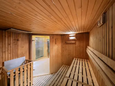 Warmer Saunaraum an Bord der MSC Divina. Wände und Decke sind mit hellem Holz verkleidet. Rechts sind gestufte Holzbänke, links der Saunaofen. Eine Glastür führt zu einem Duschbereich.
