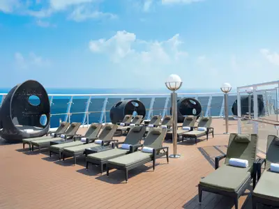 Ein sonniges Sonnendeck auf der MSC Divina mit bequemen Liegestühlen, Lounge-Pods und weitem Blick auf das offene Meer unter blauem Himmel. Ohne Personen.