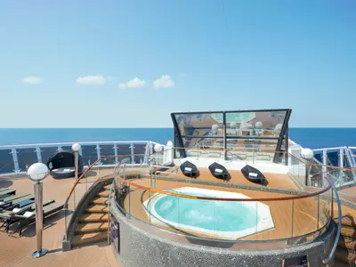 Das exklusive Sonnendeck der MSC Divina: Whirlpool, schwarze Liegen auf Holzdeck. Im Hintergrund das blaue Meer und der klare Himmel, zeugen von einer entspannten Kreuzfahrt.