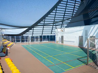 Der Sportplatz an Bord der MSC Divina. Ein überdachtes Multifunktionsfeld mit Basketballkorb, Fußballtoren und gelben Tribünensitzen. Meerblick.
