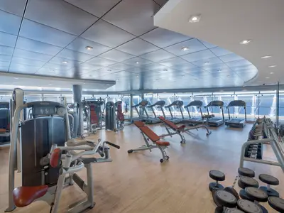 Ein helles, modernes Fitnessstudio an Bord der MSC Divina. Zahlreiche Laufbänder, Kraft- und Hantelgeräte sind zu sehen. Große Fenster bieten einen weiten Blick auf das Meer.
