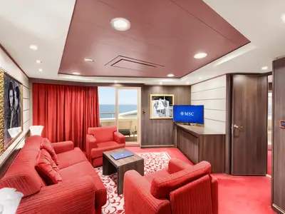 Eine elegante Suite an Bord der MSC Divina. Der Wohnbereich ist mit rotem Sofa, Sesseln, TV und Holzmöbeln eingerichtet. Ein Balkon bietet Meerblick.
