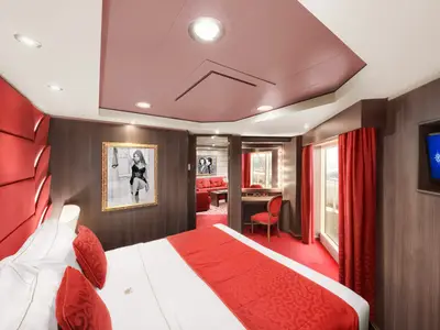 Luxuriöse Suite der MSC Divina mit großem Doppelbett, rotem Interieur, Schminktisch, Balkon und separatem Wohnbereich. Die Wände sind mit dunklem Holz verkleidet.