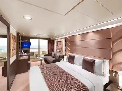 Elegante MSC Yacht Club Deluxe Suite an Bord der MSC Divina. Großes Doppelbett, Sitzecke, TV und Balkon mit Meerblick. Luxuriöse Einrichtung in warmen Farben.