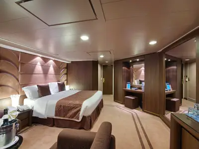Einladende und elegant eingerichtete Yacht Club Grand Suite an Bord der MSC Divina mit einem Kingsize-Bett und Champagner auf Eis.