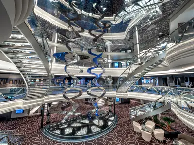 Das atemberaubende Infinity-Atrium der MSC Euribia erstreckt sich über mehrere Ebenen mit geschwungenen Treppen und einer imposanten, spiralartigen Kunstinstallation aus spiegelnden Elementen in Blau und Silber.